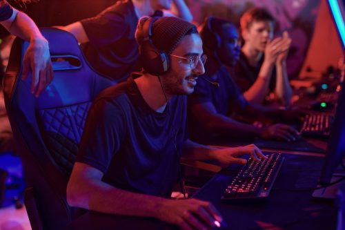 Jugadores de videojuegos en línea con cascos compitiendo en PC en una configuración de esports con iluminación de neón