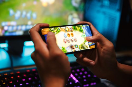 Persona jugando videojuegos en línea en un teléfono inteligente, mostrando una interfaz de juego móvil con gráficos coloridos